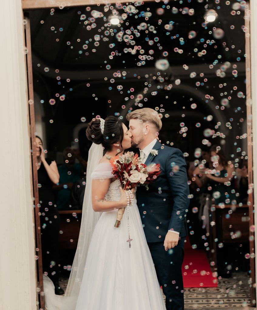 A newlywed couple shares a kiss as bubbles float around, creating a dreamy wedding moment.